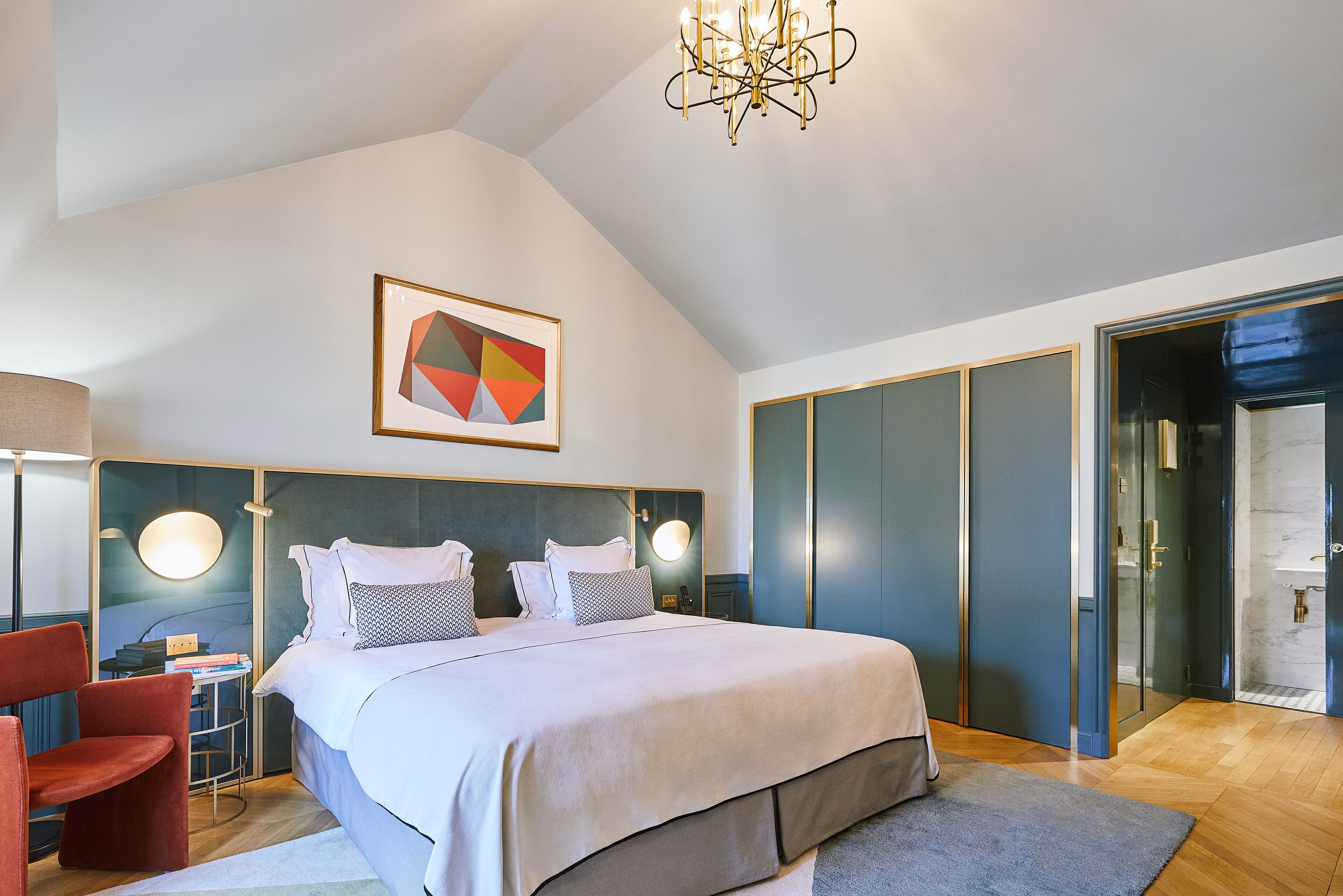 Une chambre moderne avec un grand lit, un bureau et une chaise. Un tableau orne le mur et un lustre est suspendu au-dessus du lit.