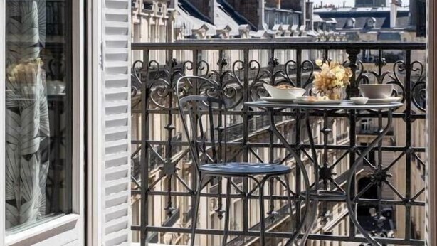 Un balcon avec vue sur la Tour Eiffel, une table avec des chaises et une fenêtre avec des stores.