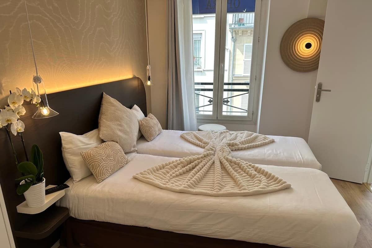 A bedroom with two beds, a potted plant, a bedside table, and a view of the outside balcony.