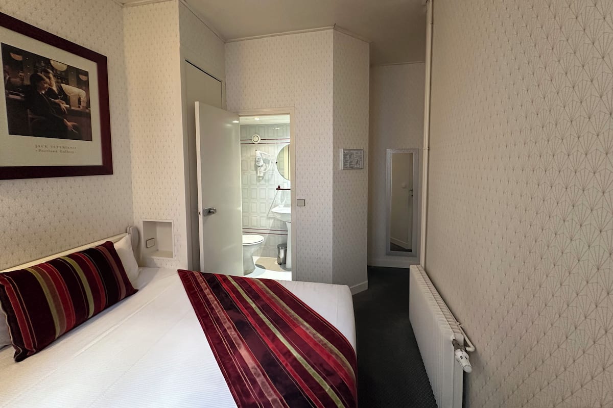 A hotel room with a bed, a framed picture on the wall, a door leading to a bathroom, and a radiator.