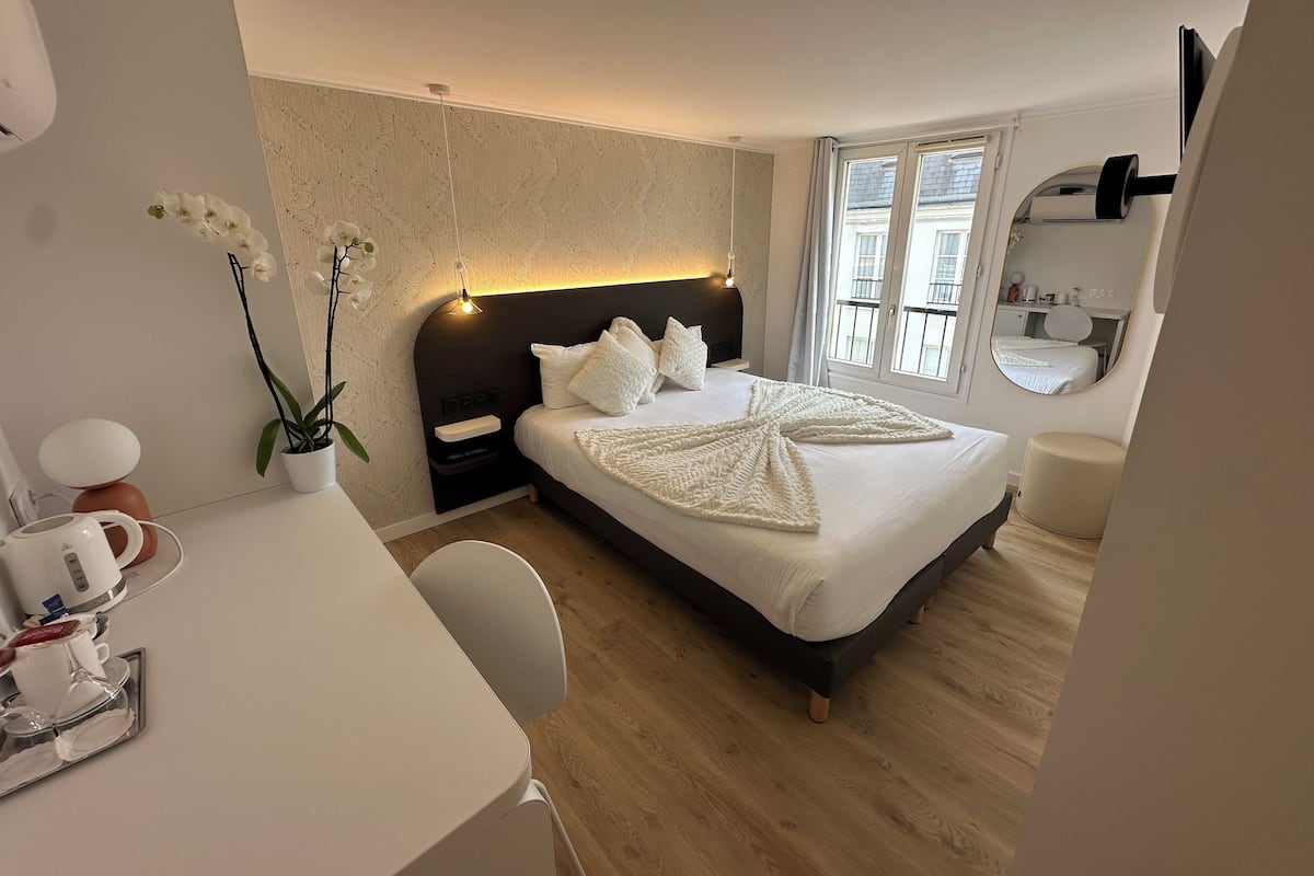 A modern hotel room with a large bed, bedside table, and a desk with a chair.