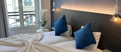 Une chambre d’hôtel moderne avec un grand lit, une vue sur la ville par la fenêtre et un panneau décoratif au mur.