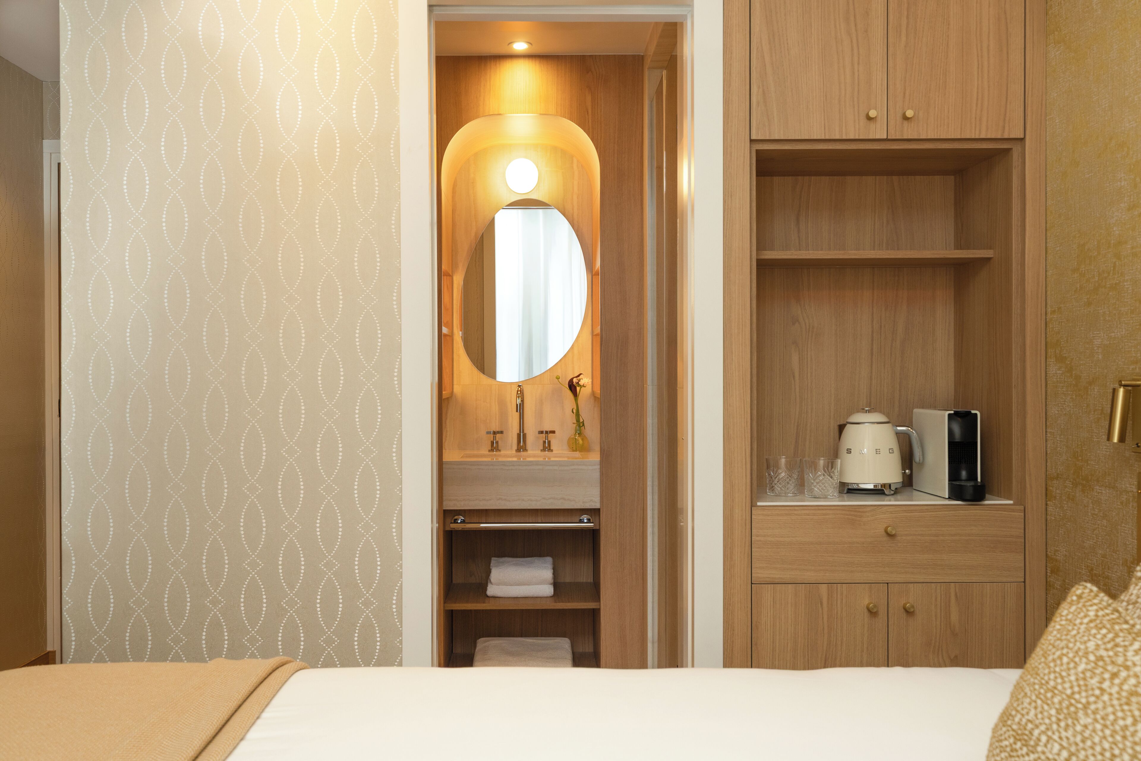 Een hotelkamer met een bed, een houten garderobe, een spiegel, een wastafel en een koffiezetapparaat.