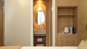Een hotelkamer met een bed, een houten garderobe, een spiegel, een wastafel en een koffiezetapparaat.