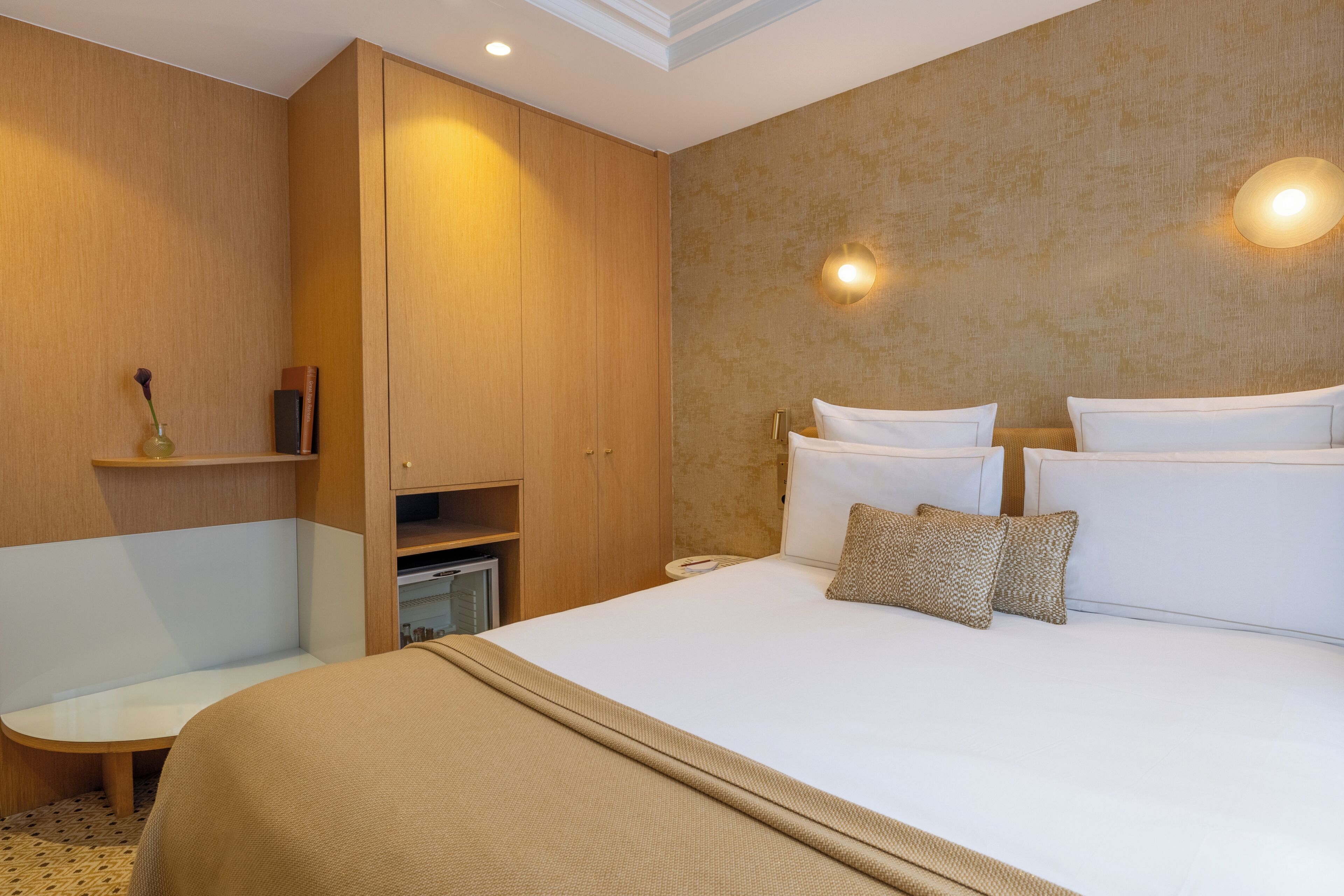 A hotel room with a bed, bedside tables, a wardrobe, and a wall-mounted light fixture.
