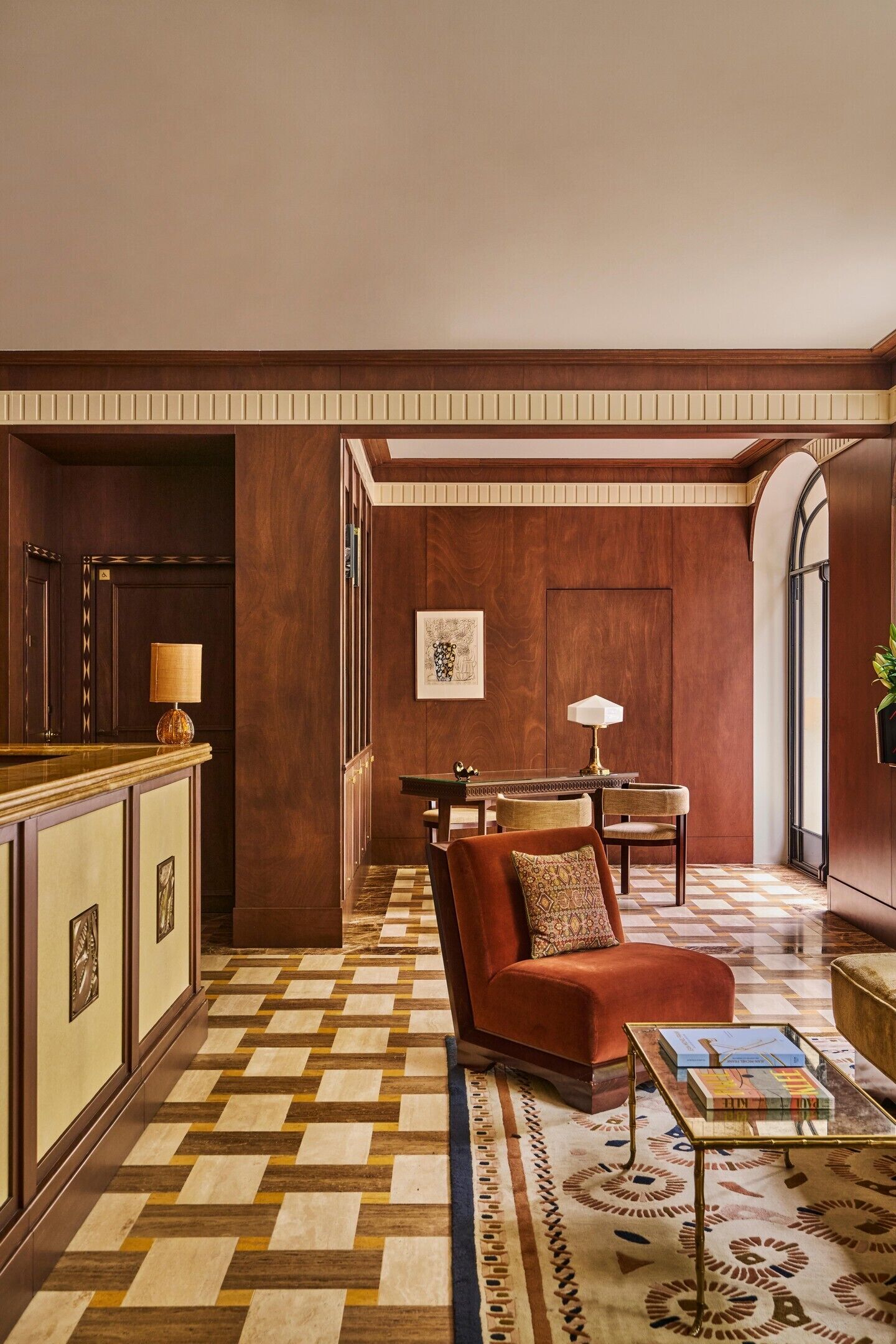 Un vestíbulo de hotel con mostrador de recepción, zona de estar con sofá y sillones, alfombra estampada y una obra de arte enmarcada en la pared.