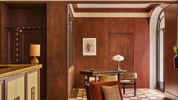 Un vestíbulo de hotel con mostrador de recepción, zona de estar con sofá y sillones, alfombra estampada y una obra de arte enmarcada en la pared.