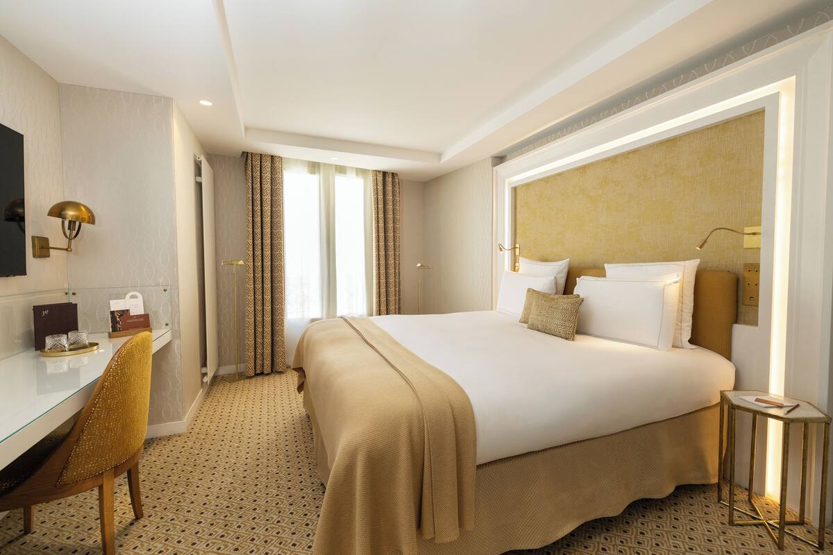 Une chambre d’hôtel avec un grand lit, un bureau, une chaise, une télévision et une fenêtre avec des rideaux.