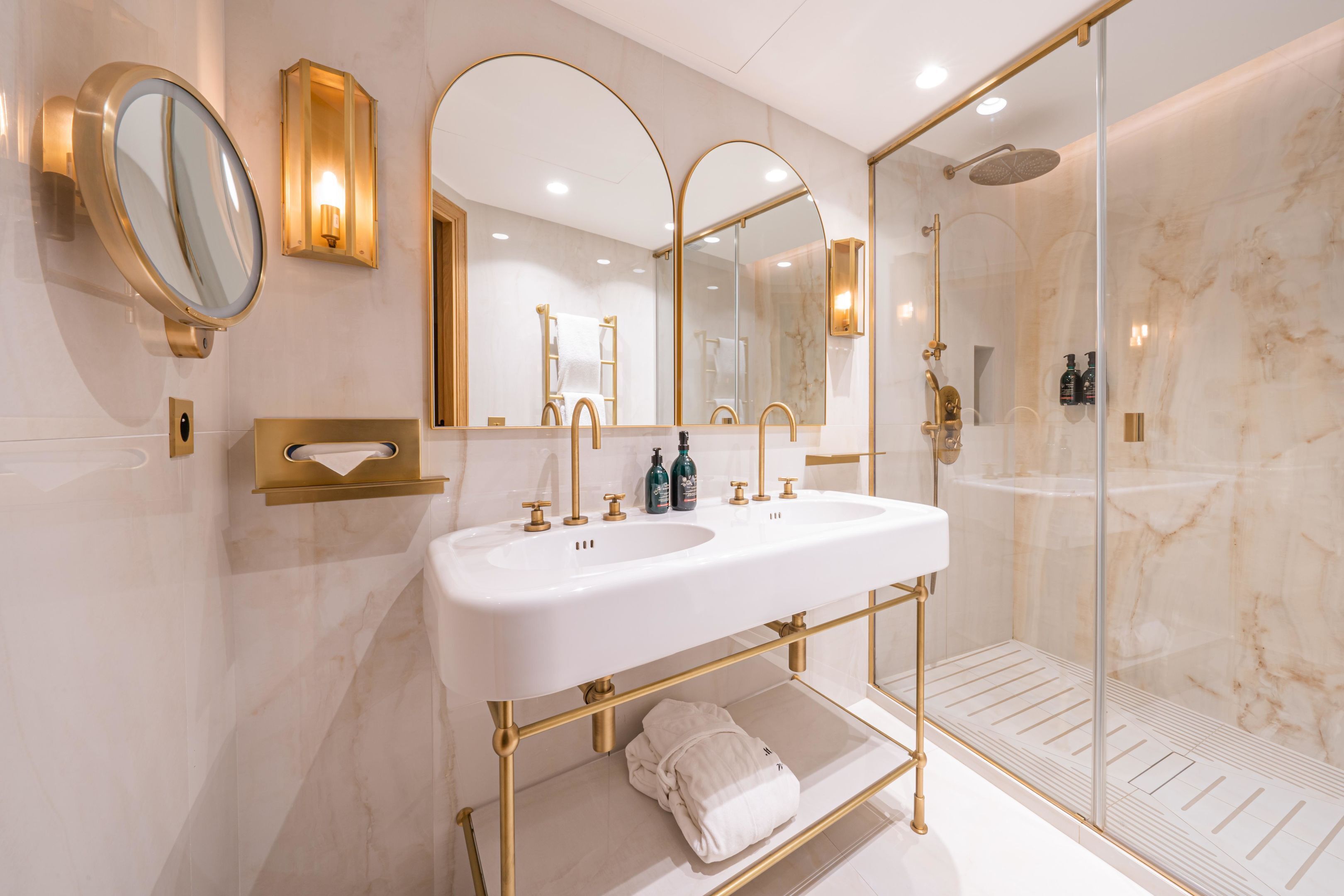 Een luxe badkamer met een groot wit wastafelmeubel, gouden details en een douche met glazen wanden.