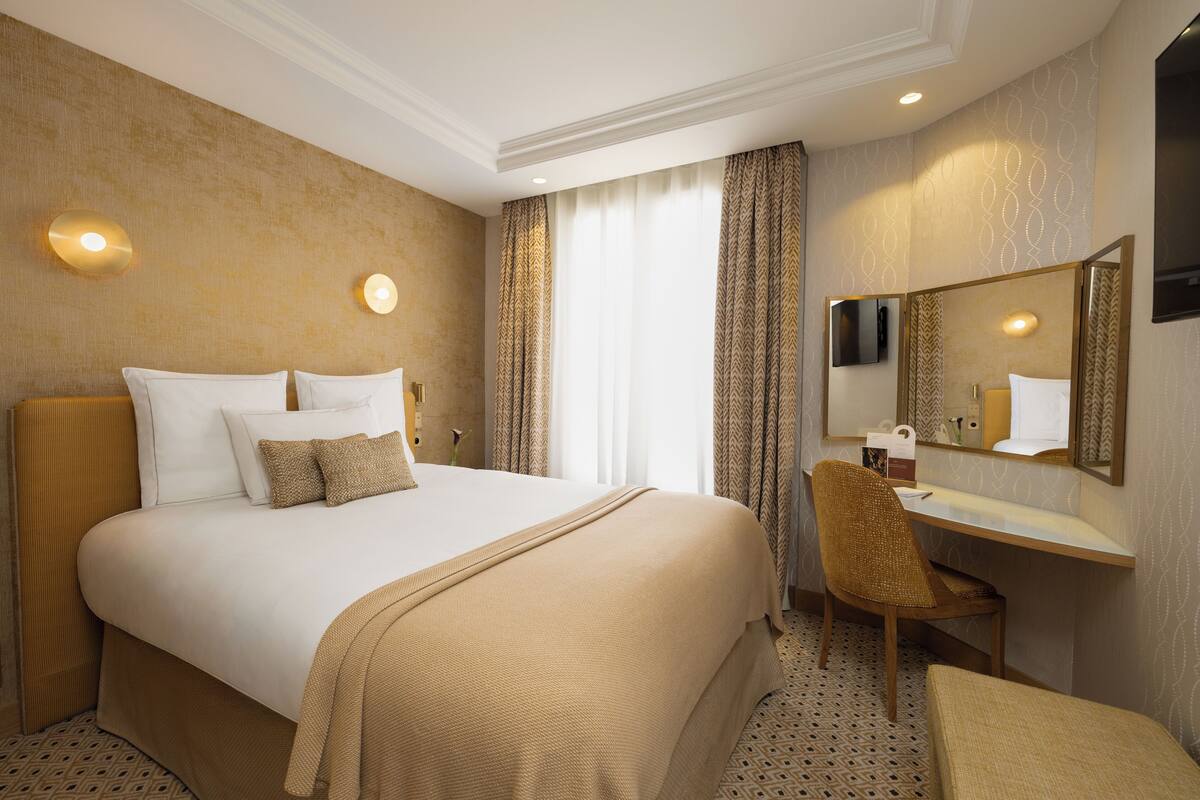 Une chambre d’hôtel avec un grand lit, un bureau, une chaise, un miroir et un téléviseur.