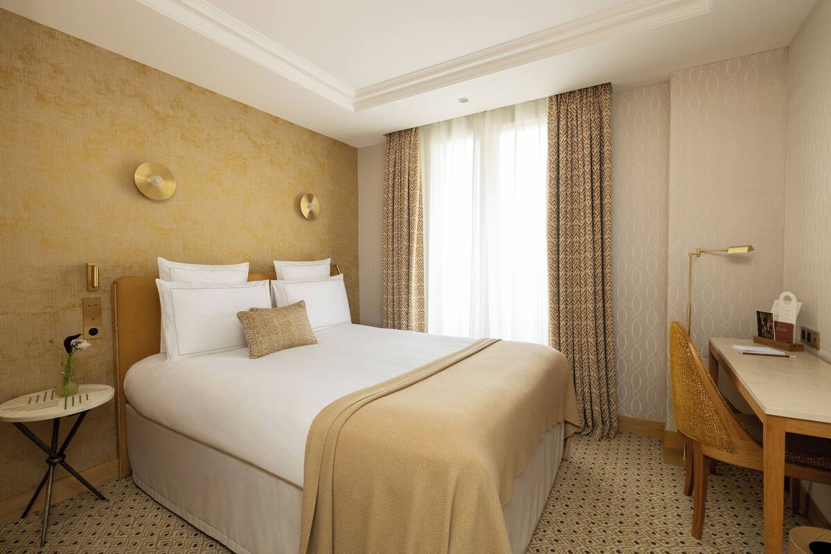Une chambre d’hôtel avec un grand lit, une petite table ronde, une chaise et un bureau avec une lampe.