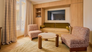 A living room with a sofa, two armchairs, a coffee table, and a TV mounted on the wall. - Hôtel Madison (Paris)