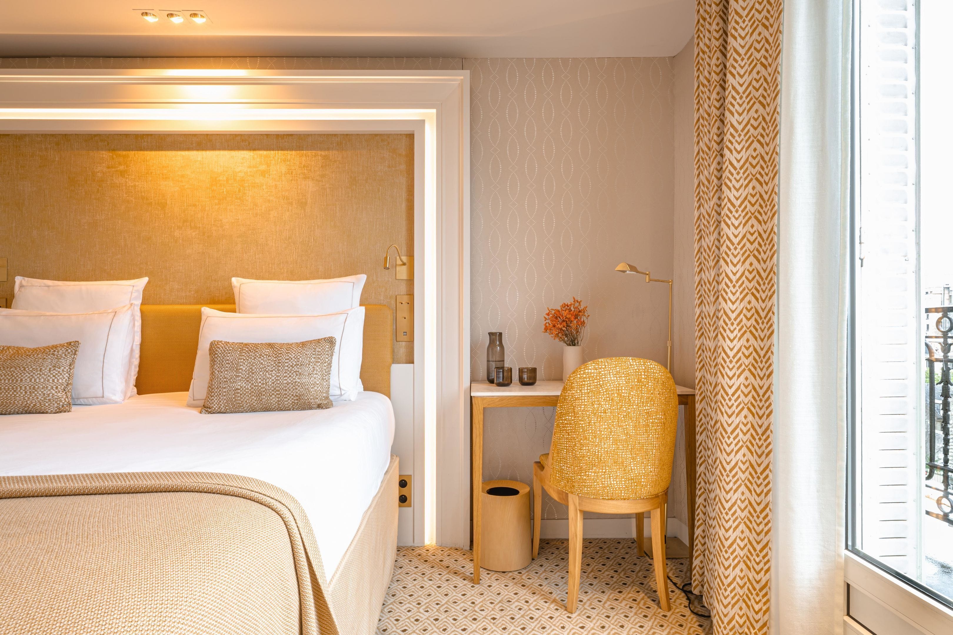 Una habitación de hotel con una cama grande, un escritorio pequeño, una silla y un ventanal con cortinas.