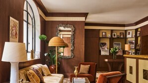 A room with a sofa, armchair, and a large mirror. There is a lamp, a plant, and a rug on the floor.