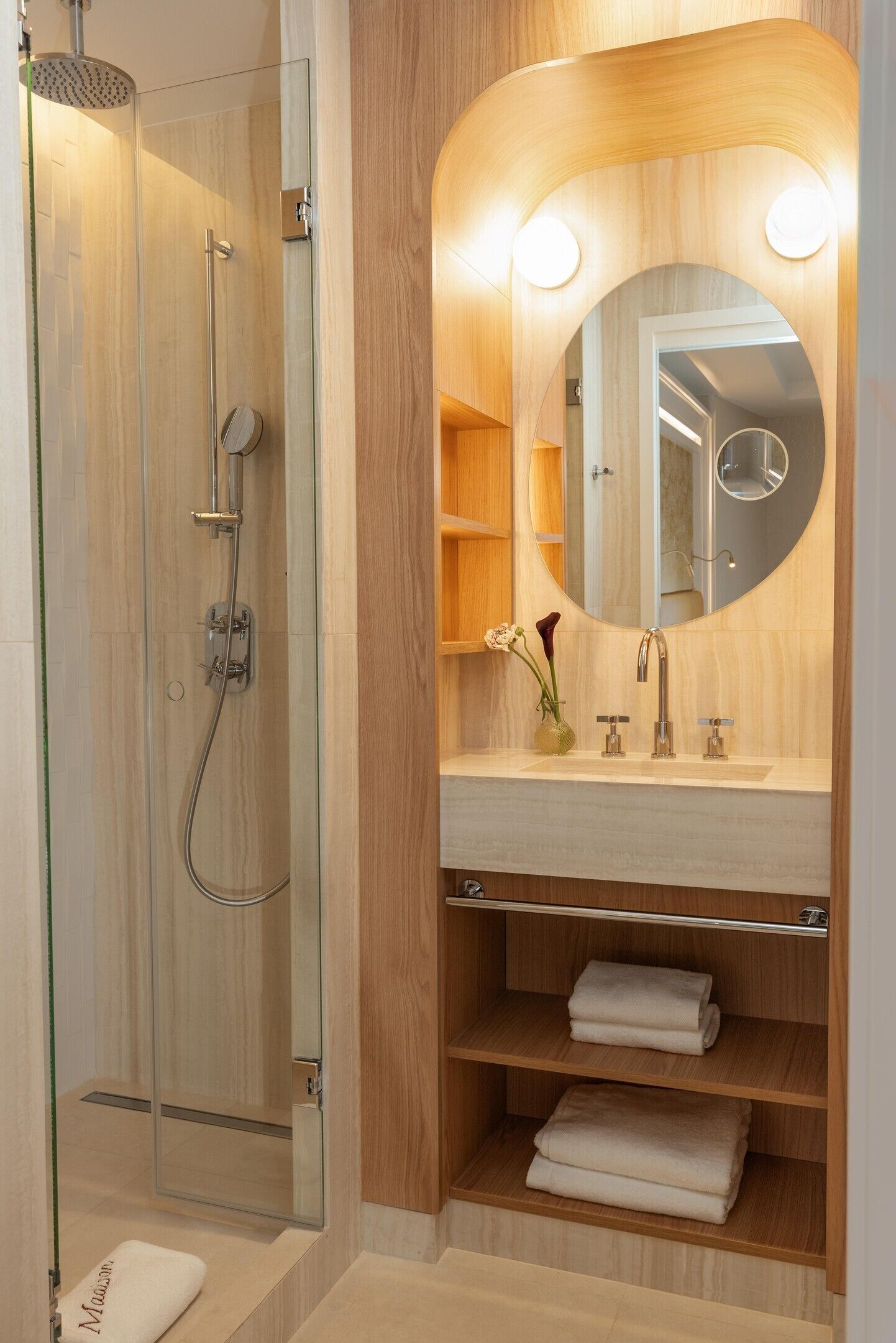 A modern bathroom with a glass-enclosed shower, a vanity with a mirror, and built-in shelves for towels.