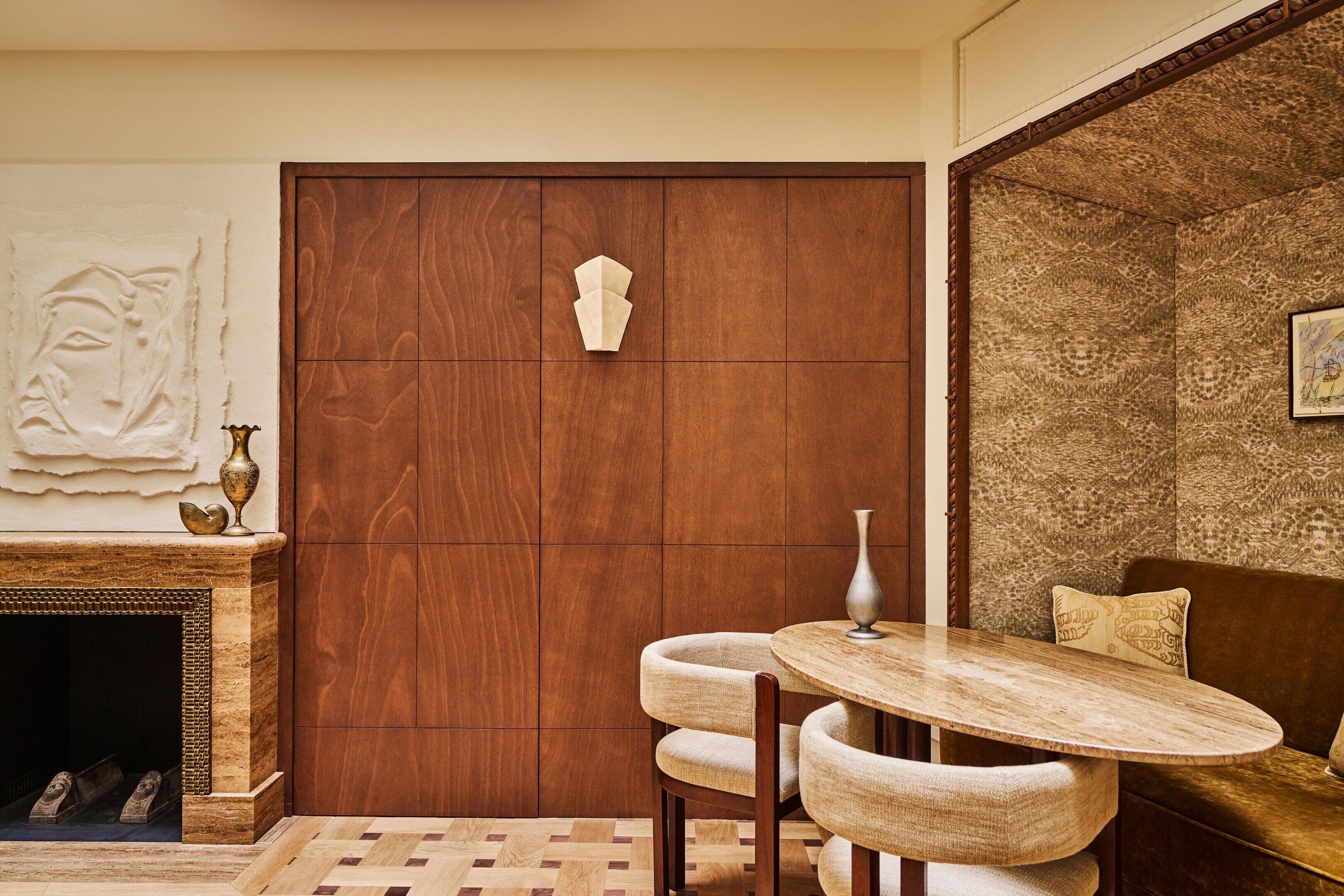 Una habitación con puerta de madera, chimenea, mesa redonda con sillas y pared decorada.