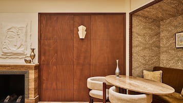 Una habitación con puerta de madera, chimenea, mesa redonda con sillas y pared decorada.