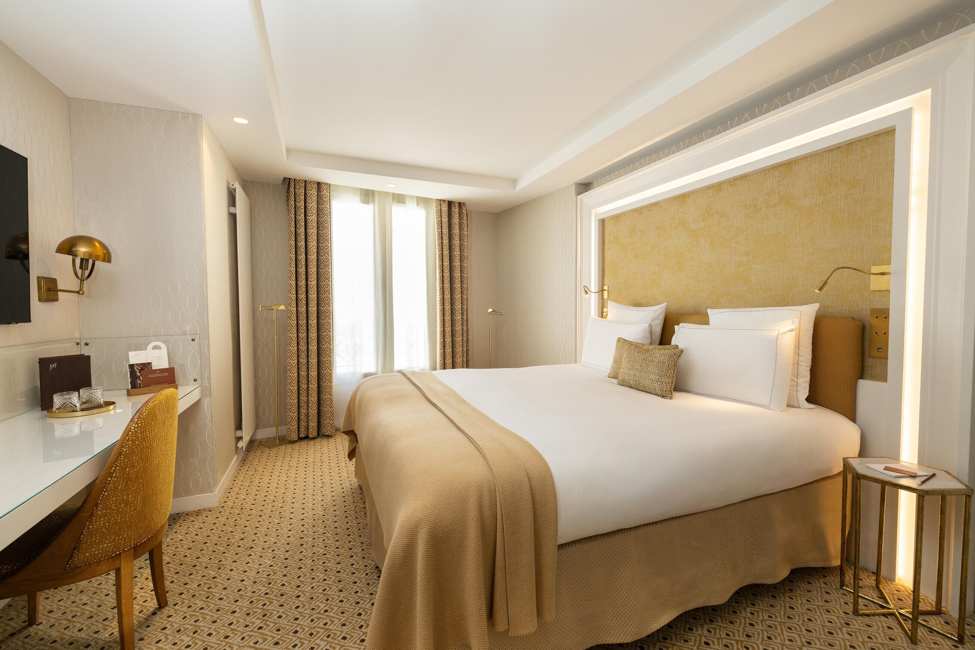 A hotel room with a large bed, a desk, a chair, and a television.