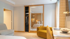 A hotel room with a bed, a sofa, a dining table with a laptop and a bowl, a closet, and a bathroom visible through an open door. - Hôtel Madison (Paris)
