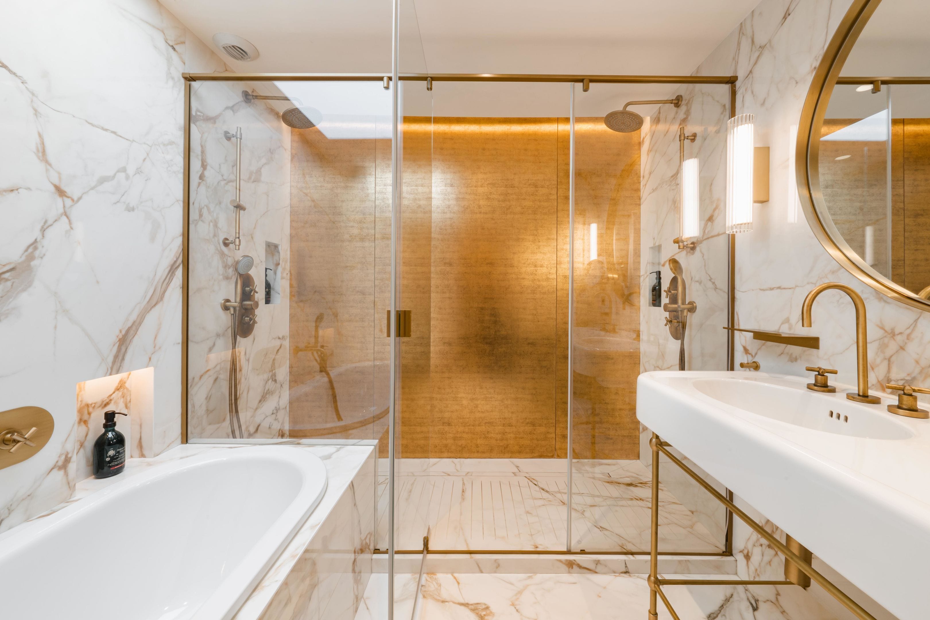 A modern bathroom with a glass-enclosed shower, a white bathtub, and a gold-framed sink.
