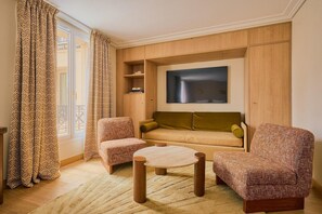 Un salon comprenant un canapé, deux fauteuils, une table basse et un téléviseur fixé au mur.