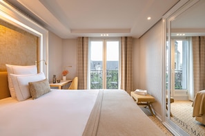 Een hotelkamer met een groot bed, een nachtkastje met een lamp, een kleine tafel met een vaas, en uitzicht op de stad door grote ramen.