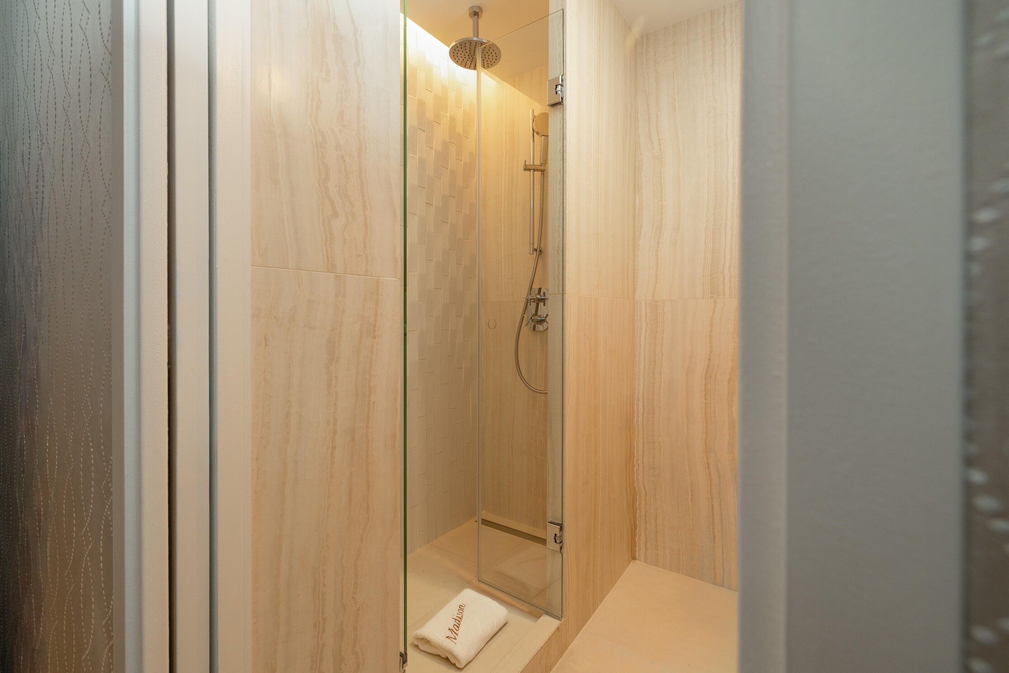 A glass-enclosed shower with a handheld showerhead and a wall-mounted faucet.