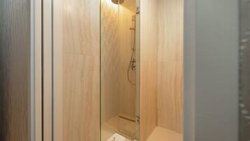 A glass-enclosed shower with a handheld showerhead and a wall-mounted faucet.