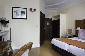Een hotelkamer met een bed, een bureau, een stoel, een foto aan de muur en een deur die naar een andere kamer leidt.