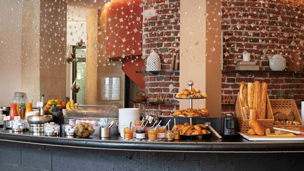 A breakfast buffet with various food items and beverages, a brick wall, and a glass display case. - Hôtel Le 123 Elysées - Astotel (Paris)