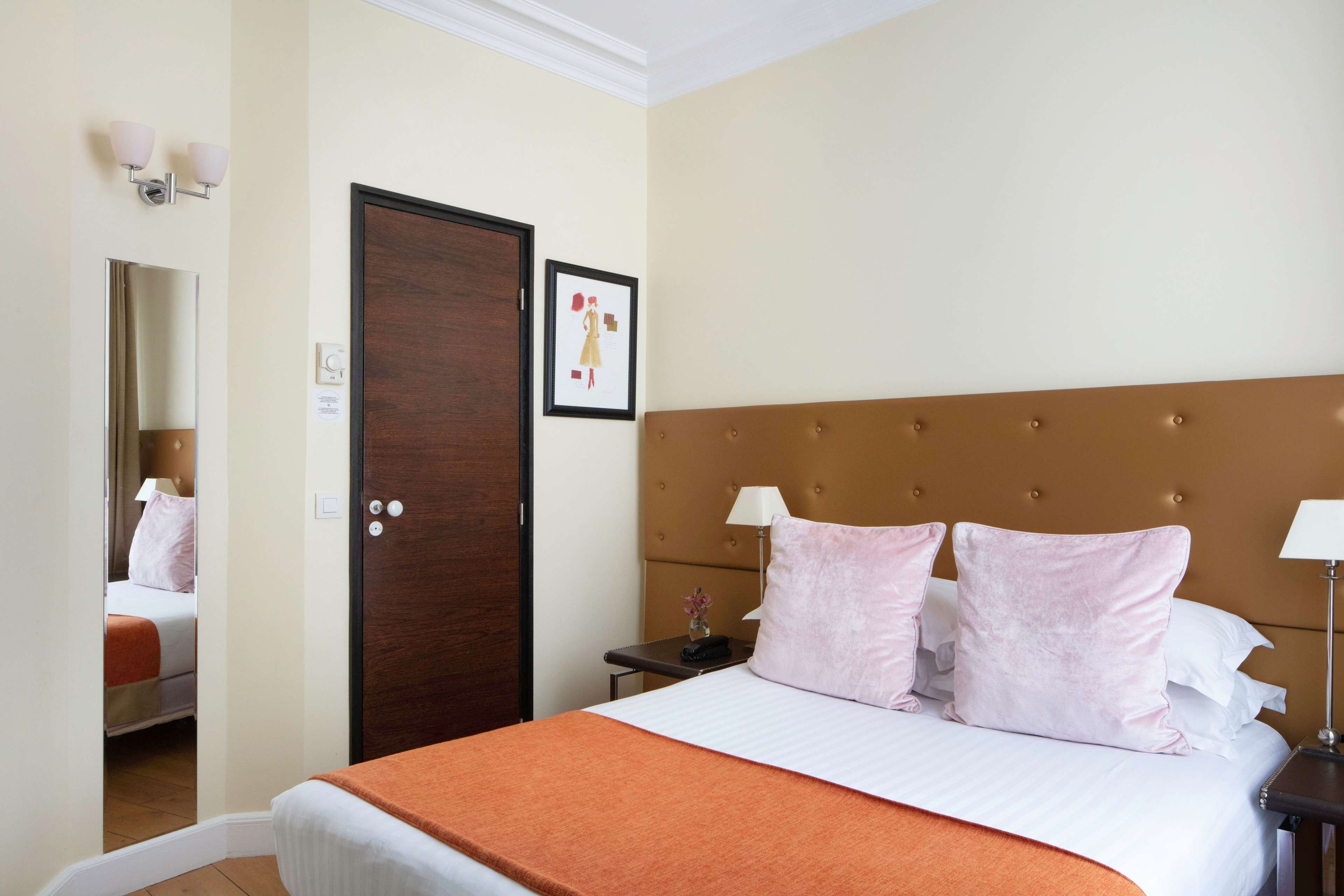 Ein Hotelzimmer mit einem großen Bett, einer Holztür, einem gerahmten Bild an der Wand und einem Nachttisch mit einer Lampe.