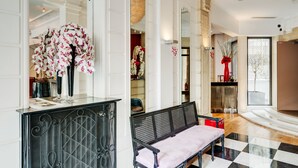 A spacious lobby with a checkered floor, a black metal bench, and a large mirror reflecting the interior. - Hôtel Le 123 Elysées - Astotel (Paris)