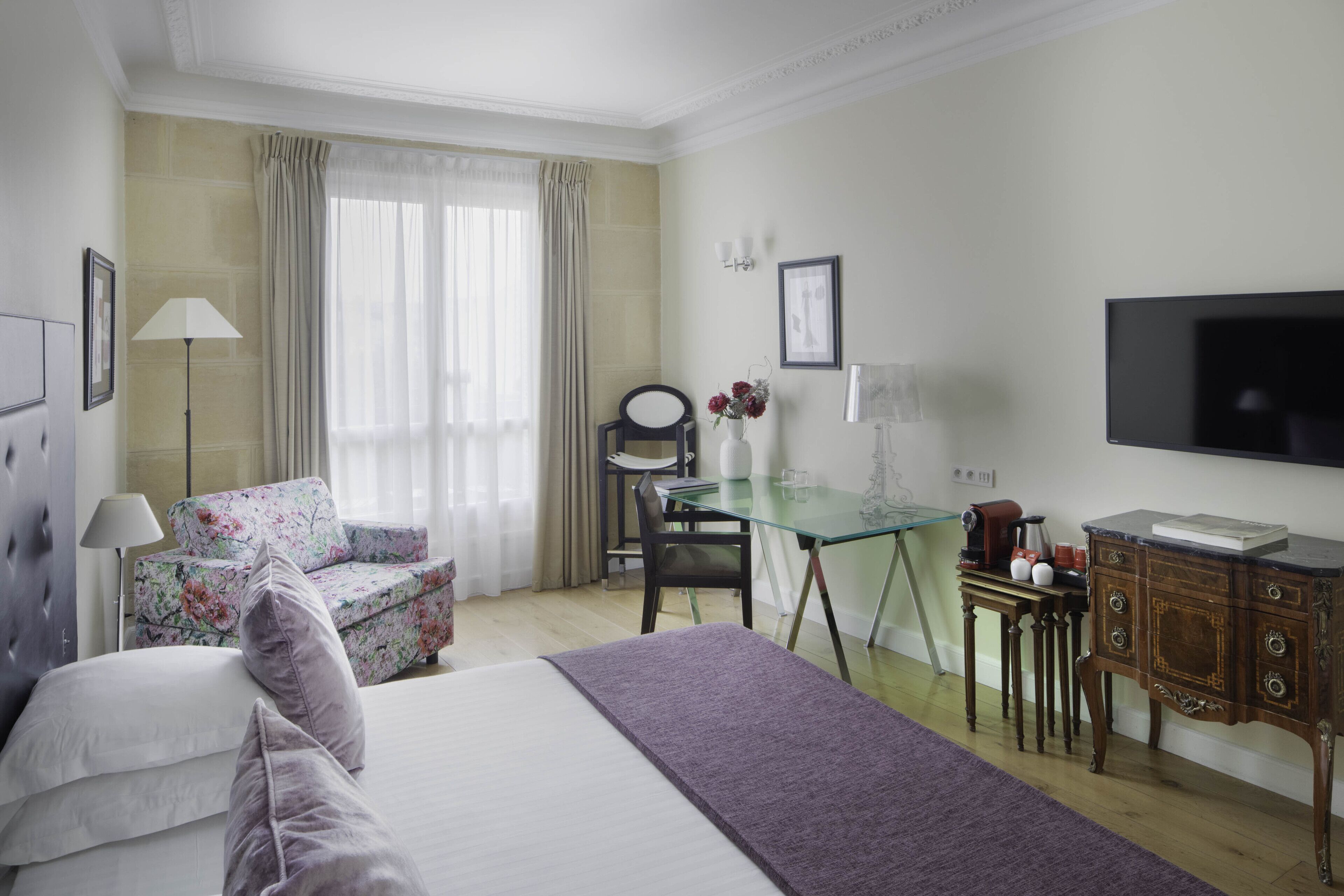 A hotel room with a bed, a desk, a chair, a TV, and a window with curtains.
