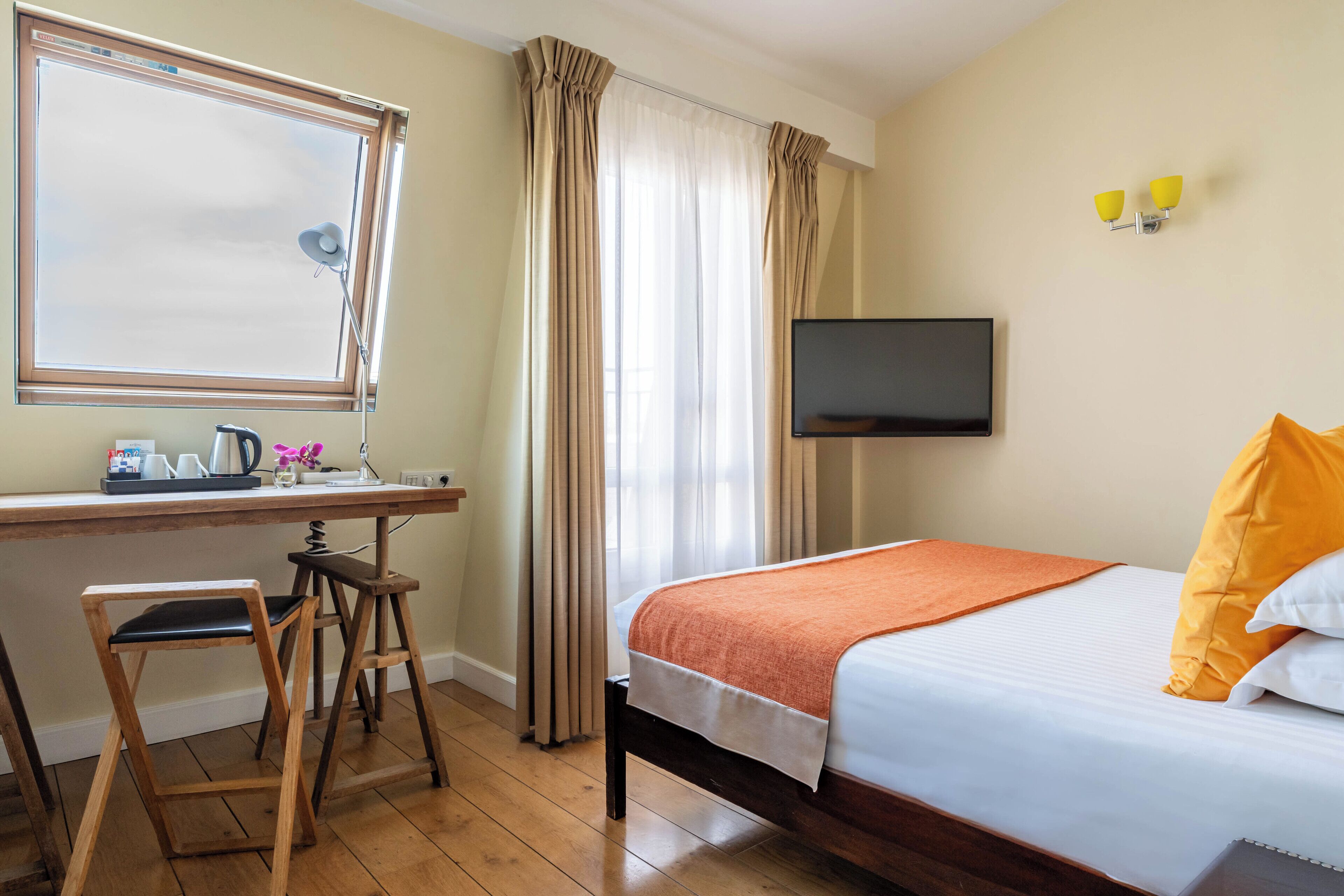 A hotel room with a bed, a desk with a chair, a television, and curtains.