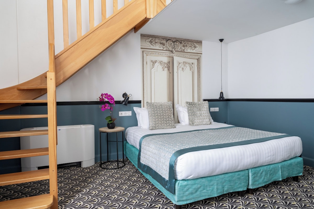 Un dormitorio con una cama, una escalera de madera, un radiador, una mesita con una planta en maceta y un panel decorativo en la pared.