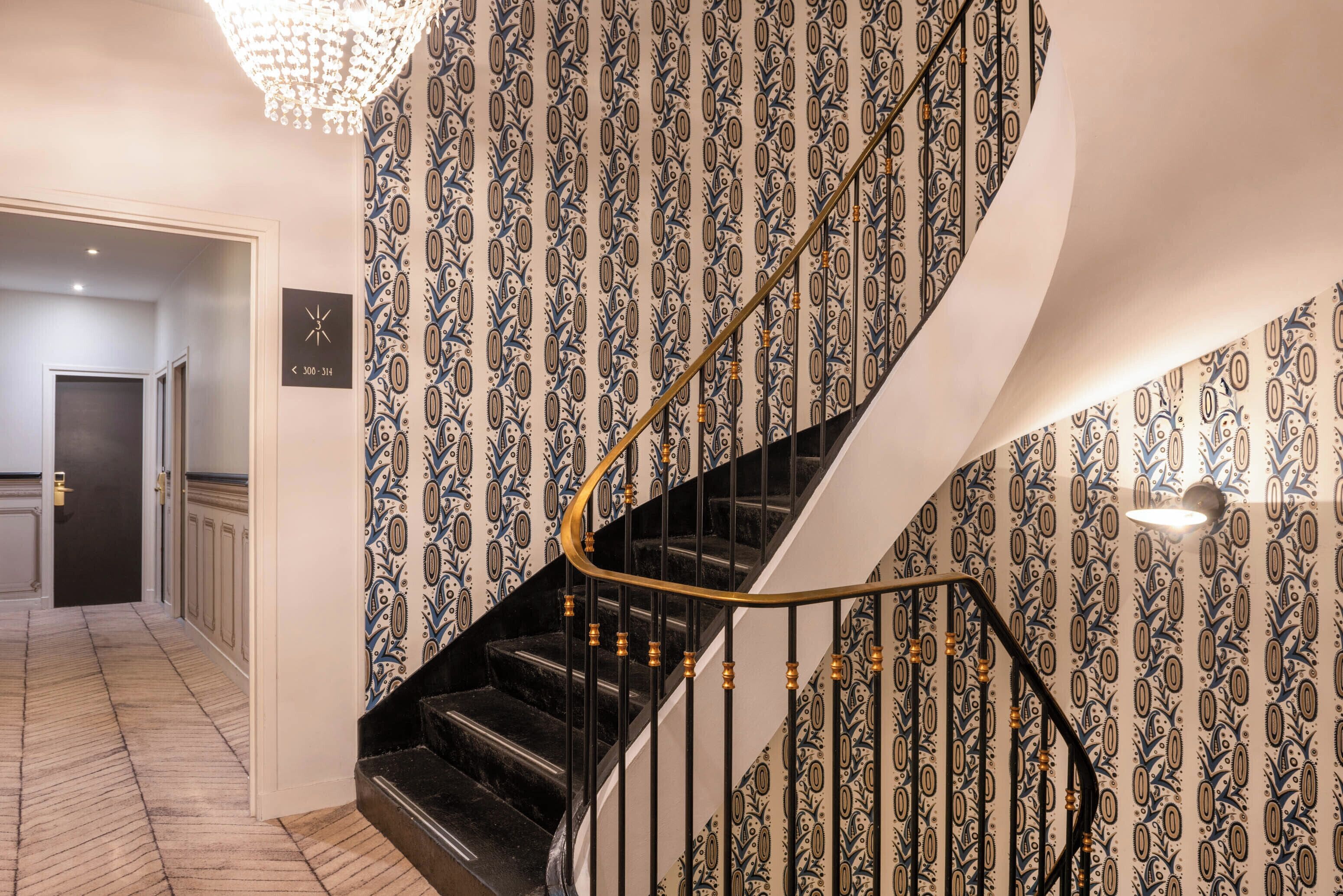 A spiral staircase with a black handrail and patterned wallpaper.