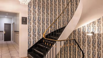 A spiral staircase with a black handrail and patterned wallpaper.