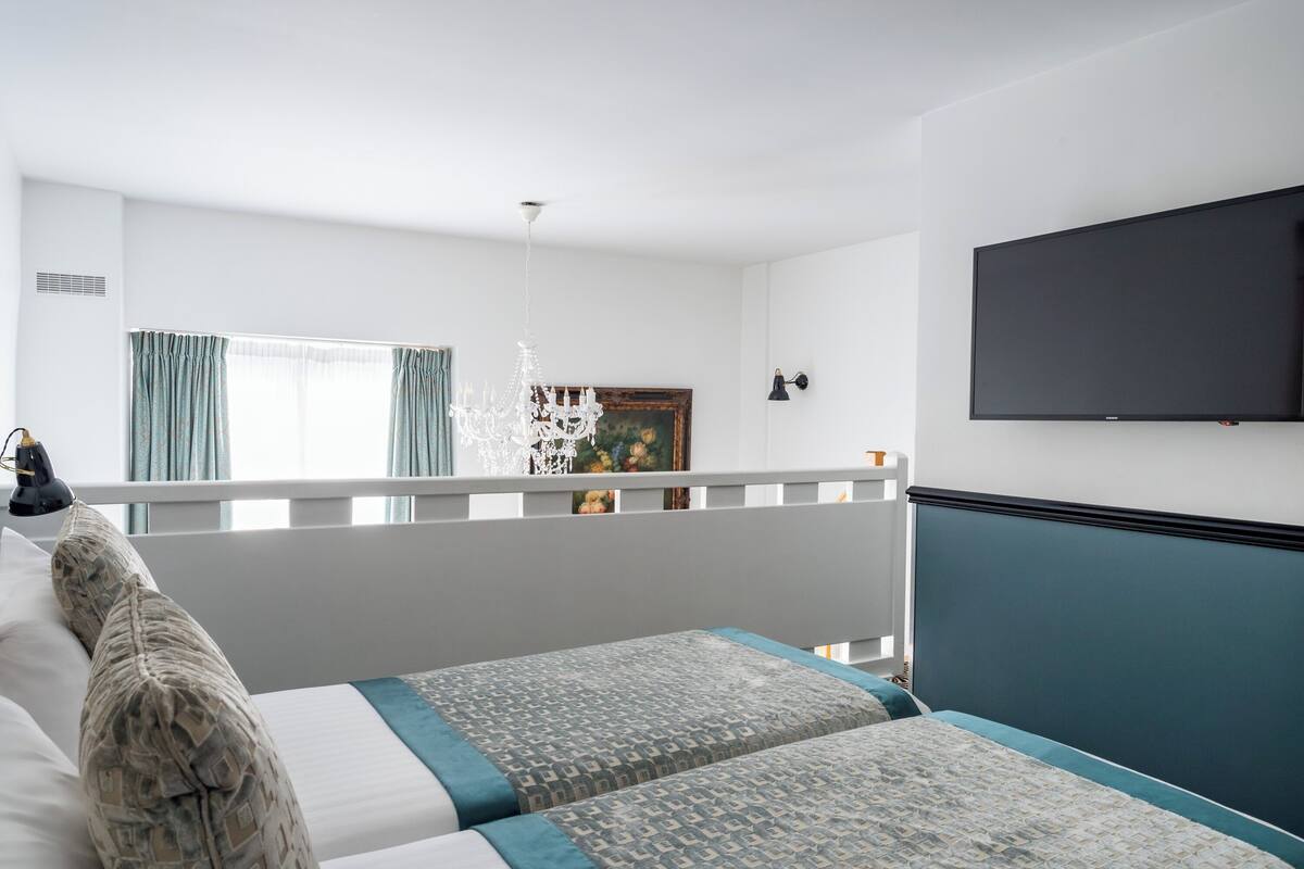 A hotel room with two beds, a TV, a chandelier, and a painting on the wall.