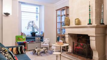 A cozy living room with a fireplace, a bookshelf, a window with blinds, a sofa, and a small table.