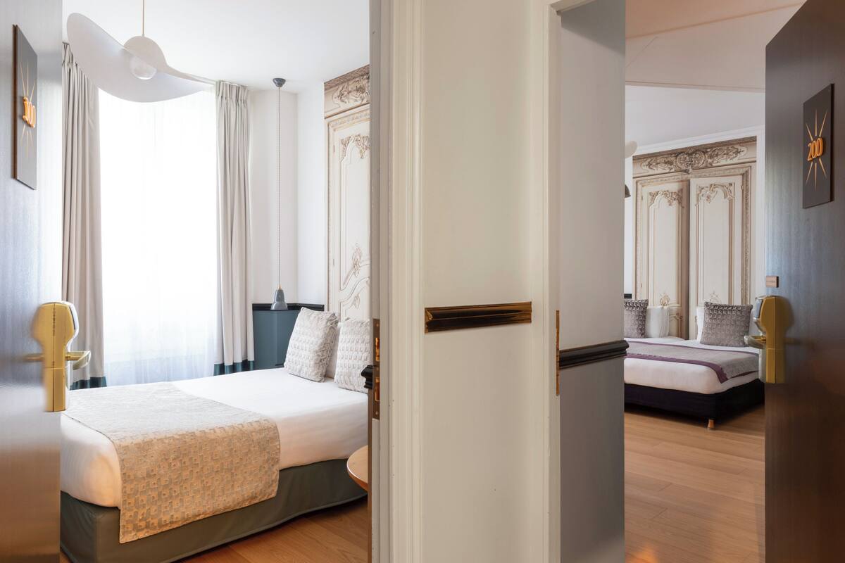 A hotel room with a large bed, a bedside table, a wall-mounted clock, and a door leading to another room.