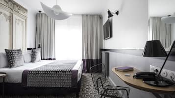 A modern hotel room with a large bed, a desk with a lamp, a chair, and a large mirror.