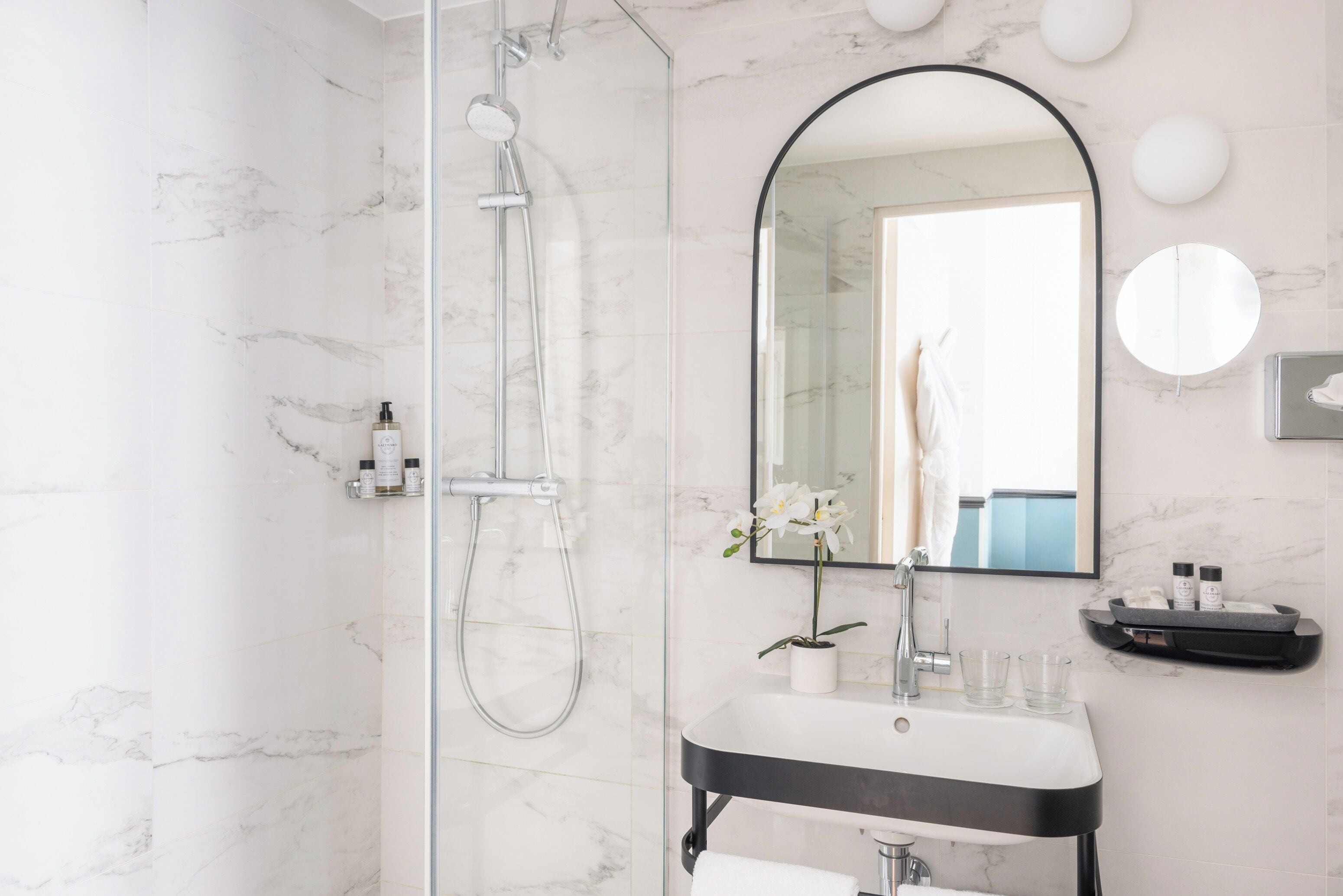 A modern bathroom with a glass-enclosed shower, a large mirror, and a sink with toiletries.