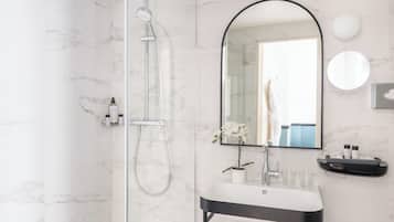 A modern bathroom with a glass-enclosed shower, a large mirror, and a sink with toiletries.