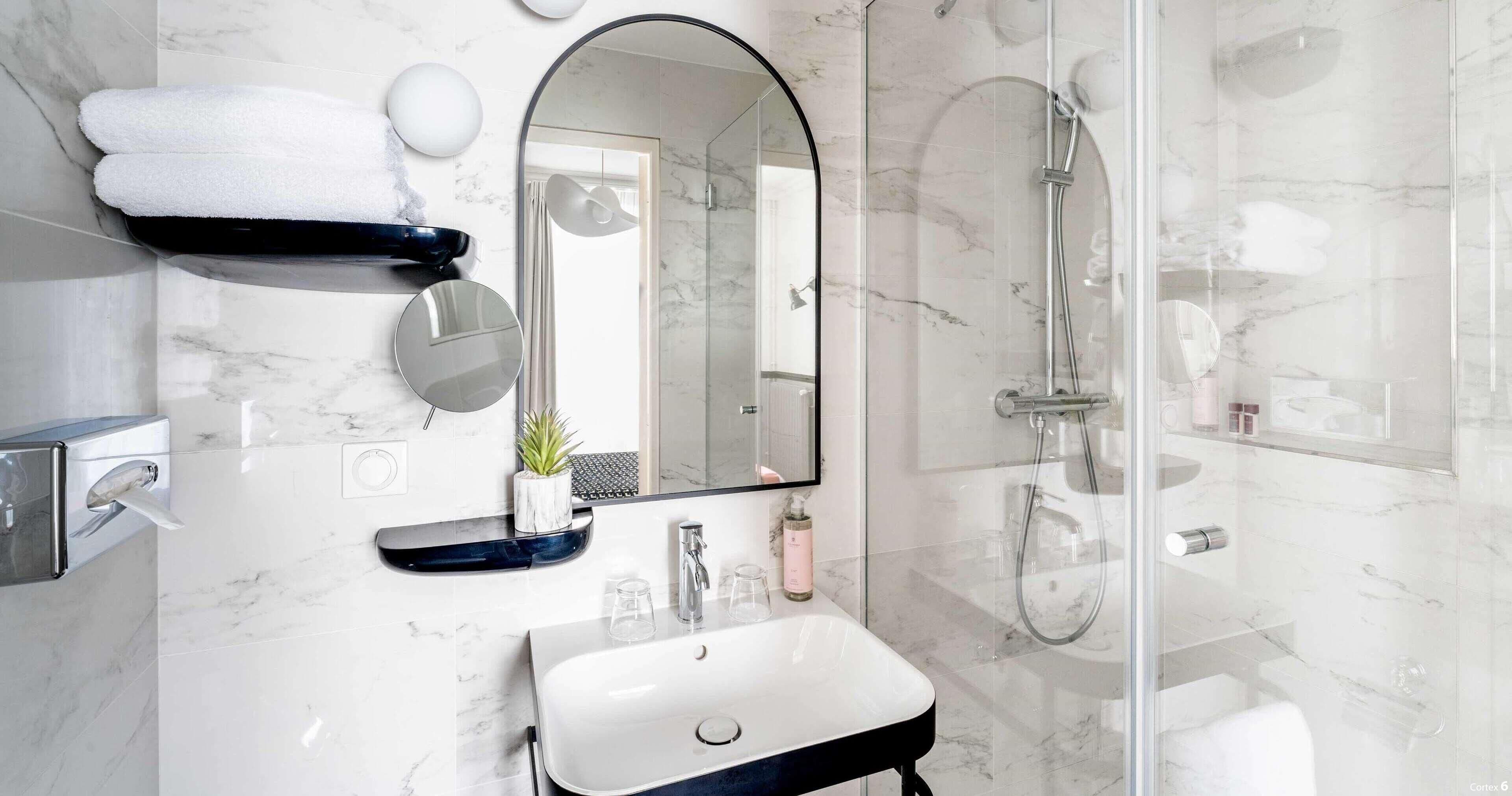Une salle de bain moderne avec un lavabo en marbre, un grand miroir, une douche en verre et des serviettes soigneusement rangées.