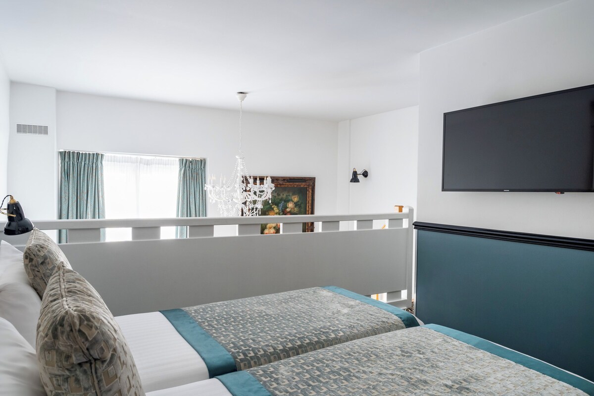 Une chambre d’hôtel avec deux lits, un téléviseur, un lustre et un tableau au mur.
