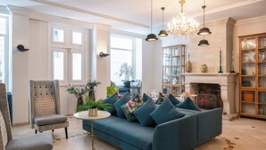 Una sala de estar con un sofá azul, un sillón estampado, una mesa de centro redonda y una chimenea.