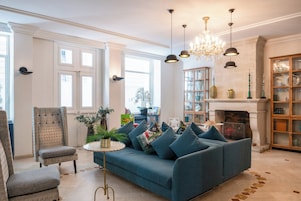 Un salon avec un canapé bleu, un fauteuil à motifs, une table basse ronde et une cheminée.