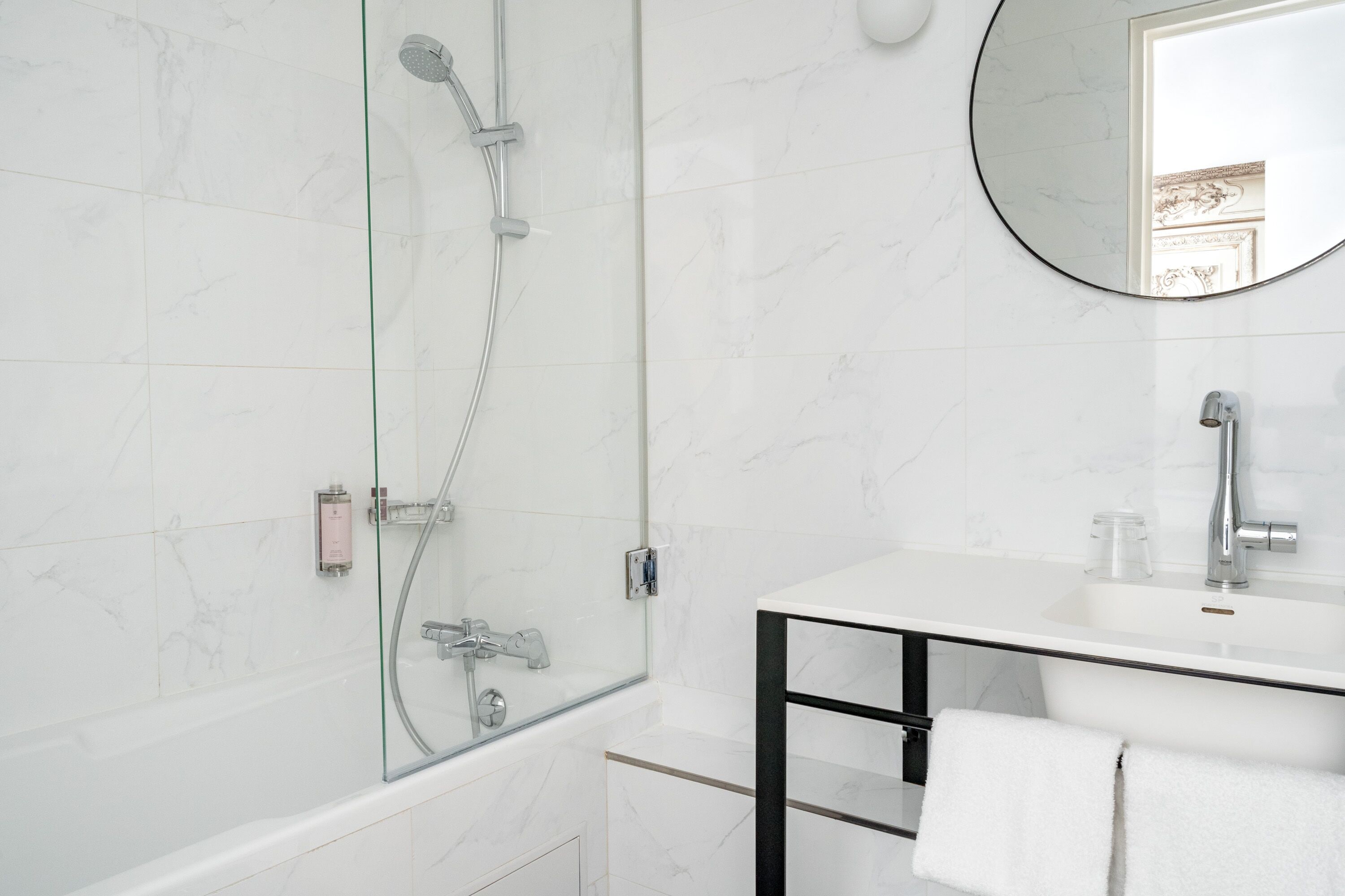 A modern bathroom with a glass-enclosed shower, a white sink with a black frame, and a round mirror.