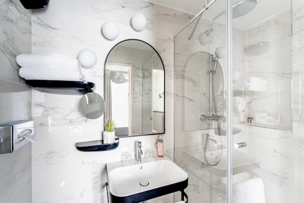 A modern bathroom with a marble wall, a large mirror, a sink, and a glass-enclosed shower.