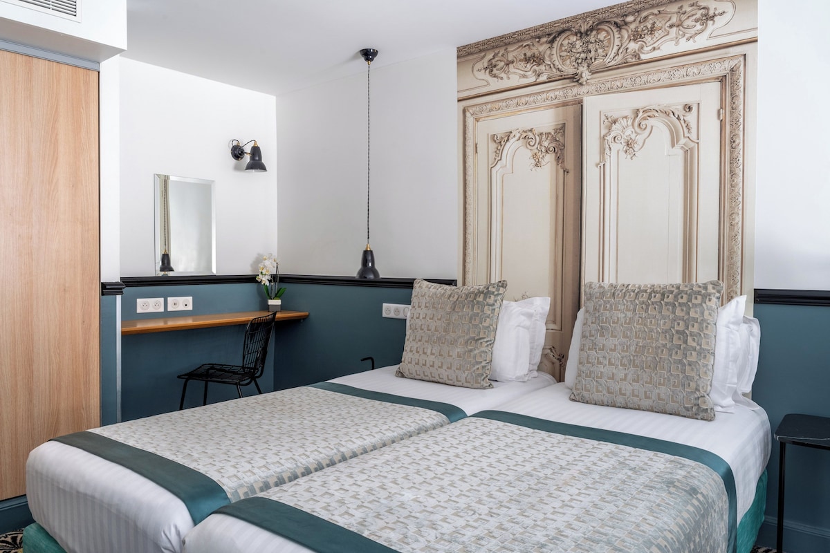 A double bed with a patterned bedspread, a bedside table, a mirror, and a decorative headboard.